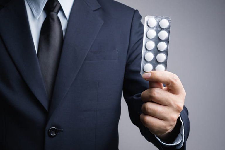 Imagen decorativa abstracta donde se ve un hombre con traje que sujeta un envase de medicamentos con 10 pastillas redondas y blancas