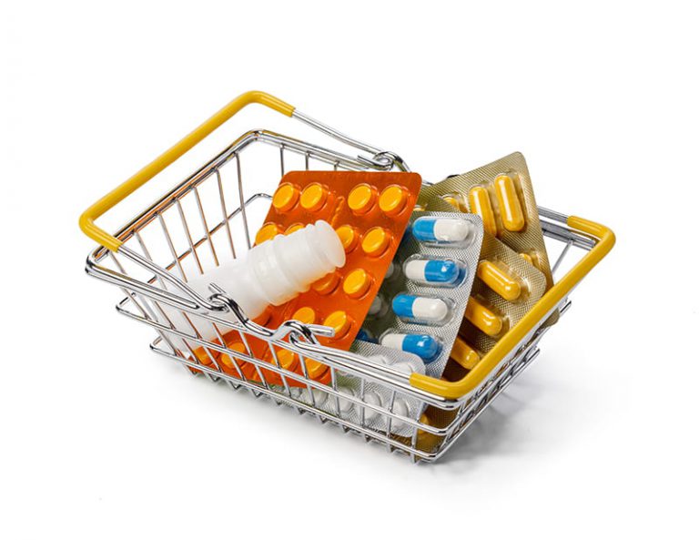 Imagen decorativa donde se ve una pequeña cesta de la compra de metal que contiene varios envases de medicamentos de diferentes formas y colores